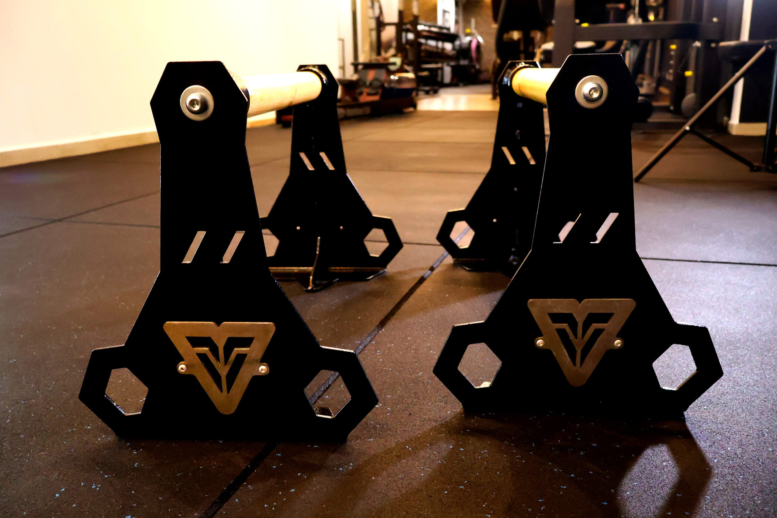 Rear view of Veevon Wooden High Pro Parallettes featuring a black steel frame, stainless steel logo and premium bright wood handles on a gym floor